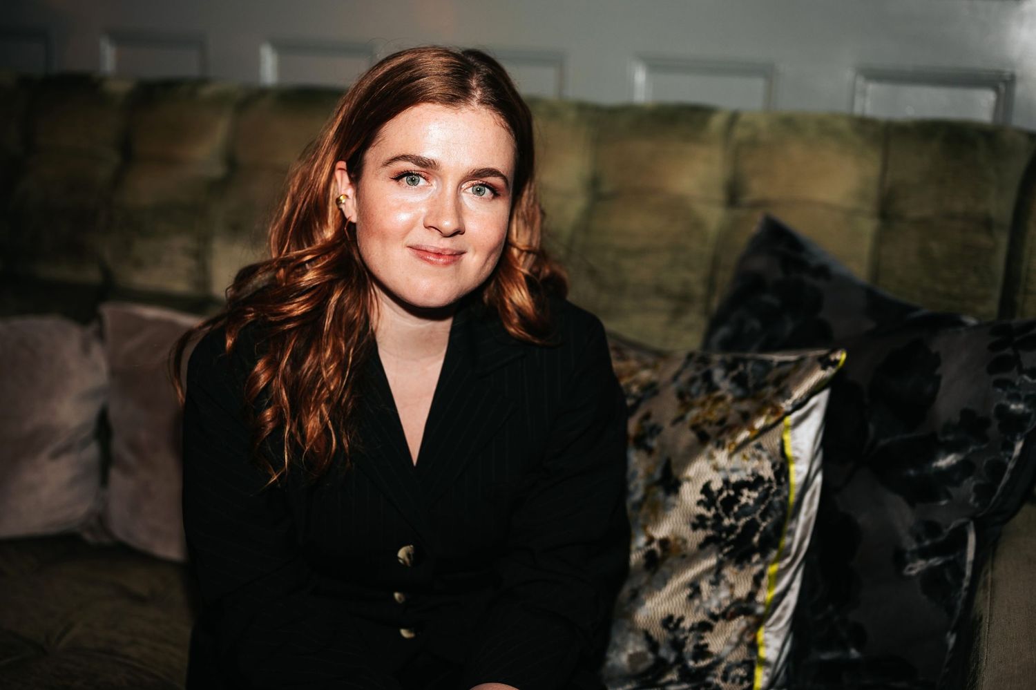 Portrait against dark background wearing black blazer with auburn hair.