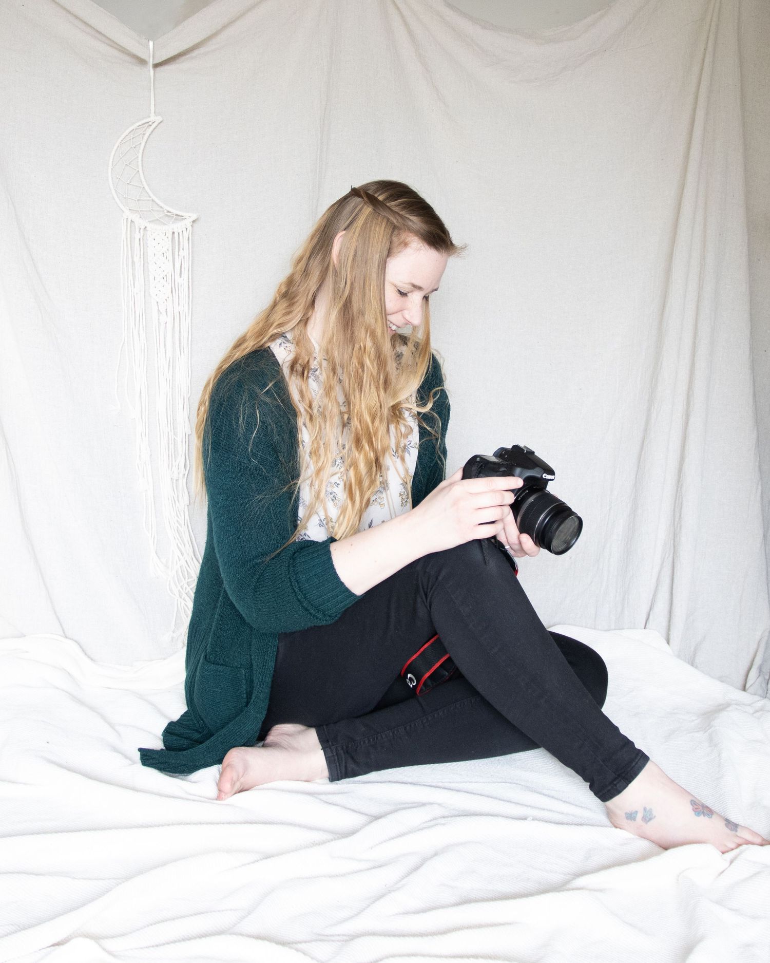 A friendly looking photographer looking at her camera. in a relaxed pose on a cream boho inspired backdrop.