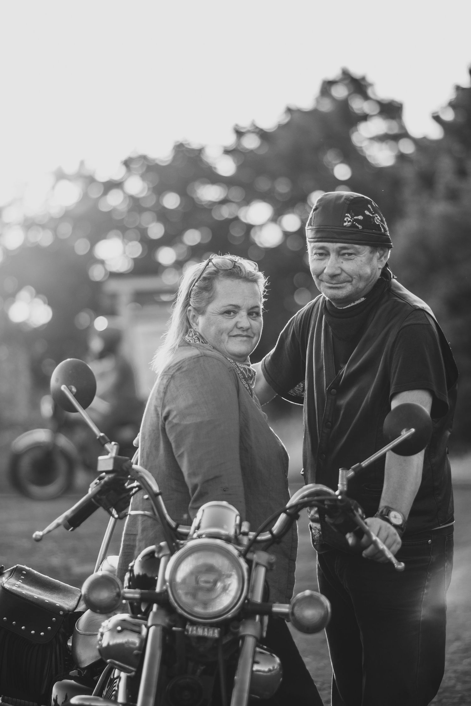 Couple posing together with a motorcycle at sunset, creating a nostalgic outdoor scene.