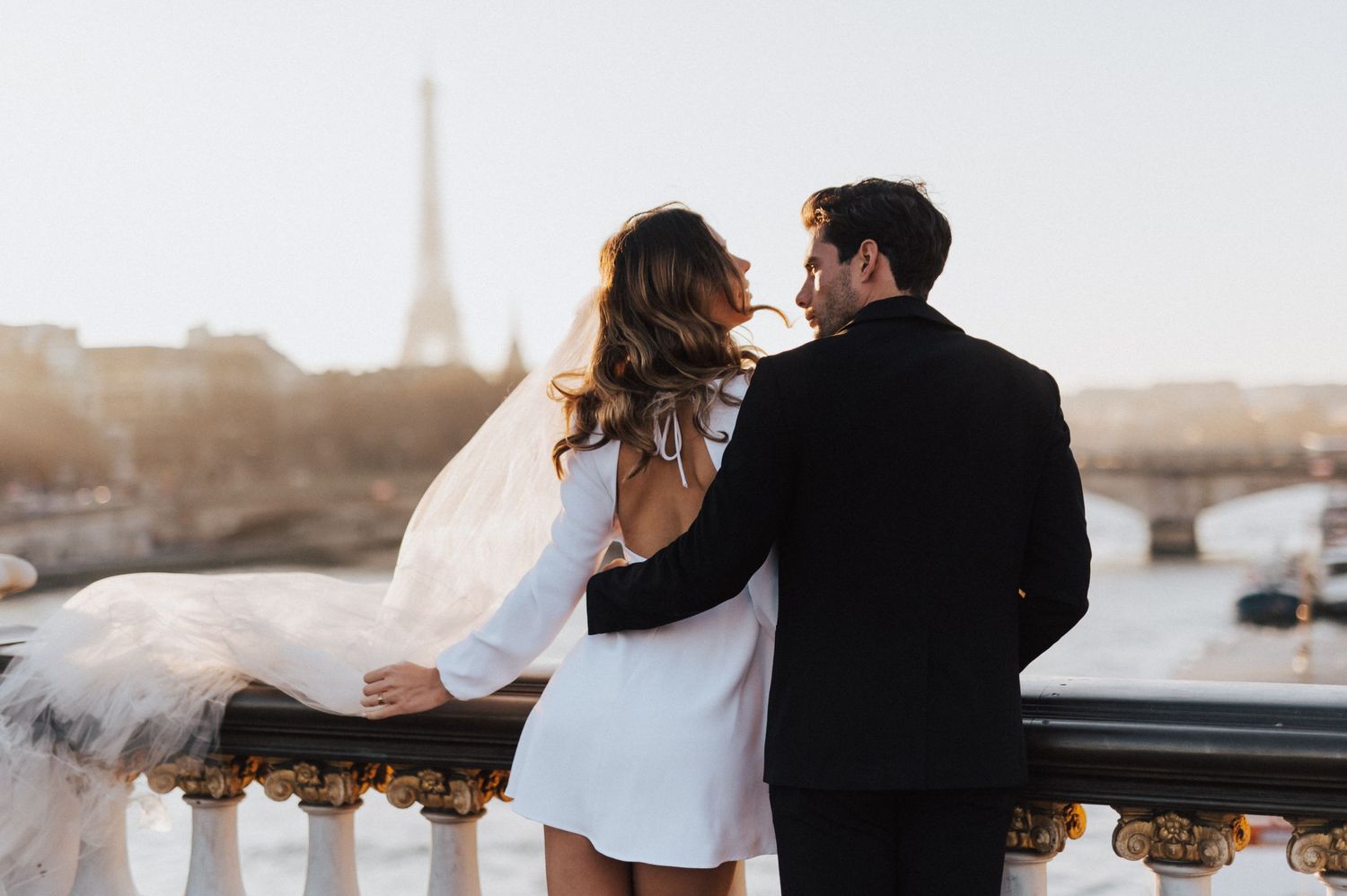 A romantic couple embracing on a Parisian balcony with the Eiffel Tower visible in the distance.