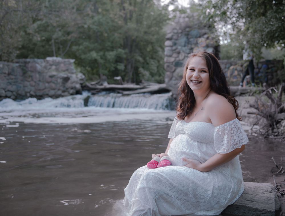 A joyful maternity portrait by a waterfall featuring a white lace dress.