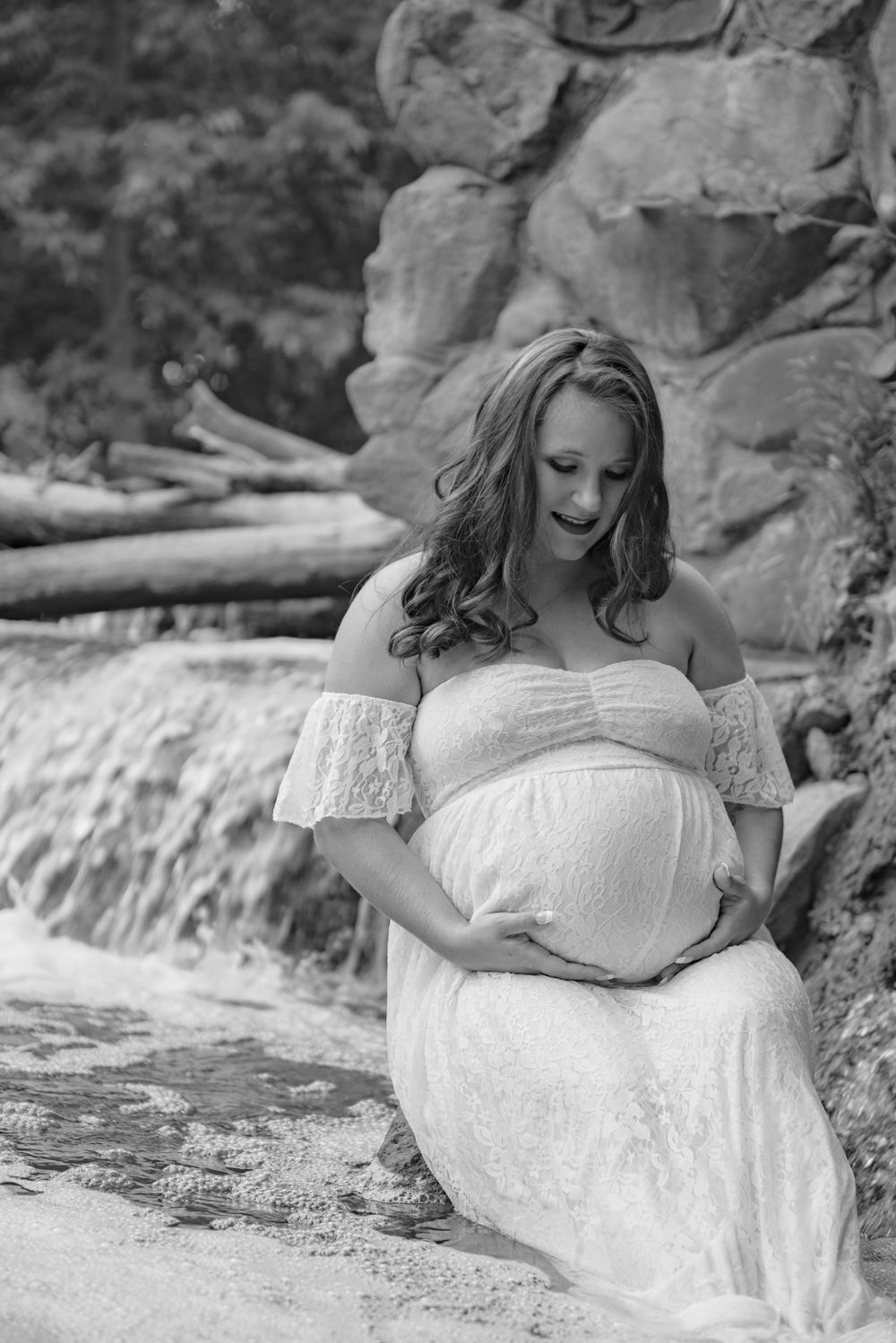 Maternity photo shoot in a white lace dress against rocky backdrop in black and white.