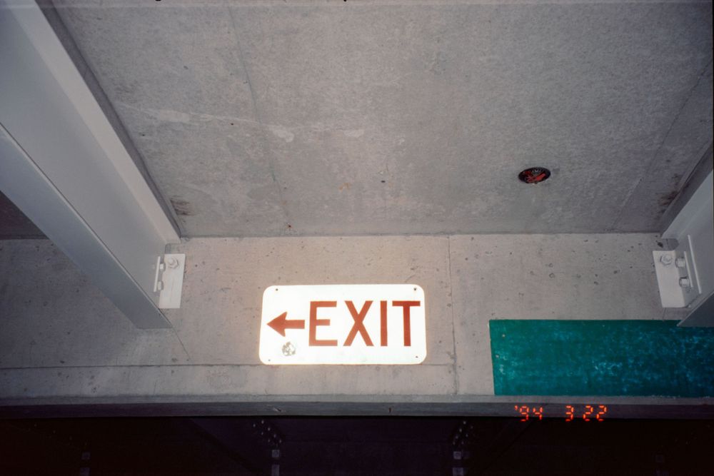 Red illuminated exit sign mounted on concrete ceiling.