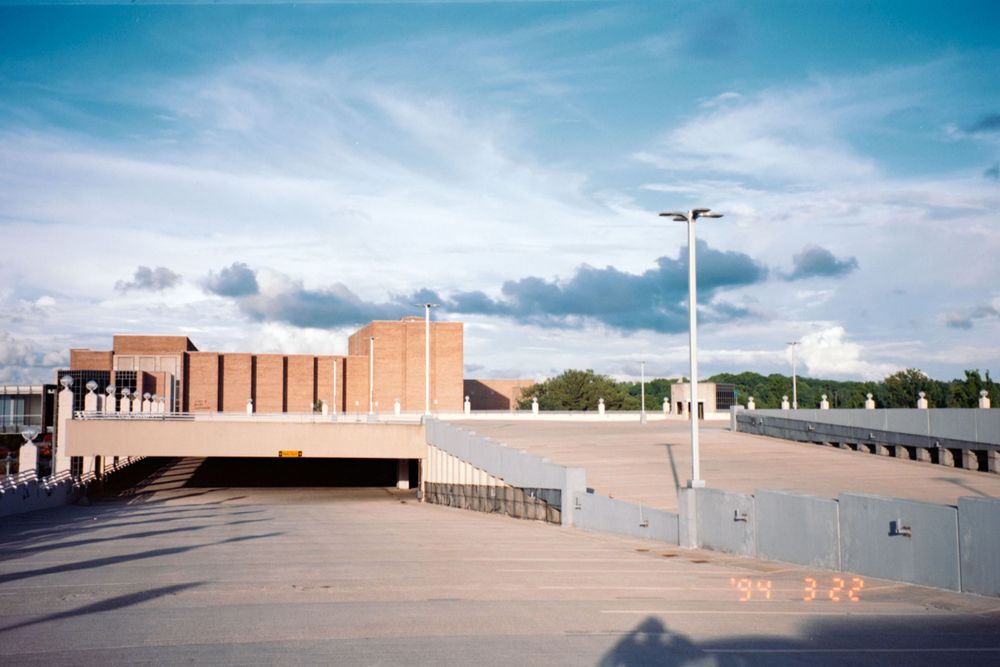 Panoramic view of a parking lot and buildings under a cloudy blue sky.