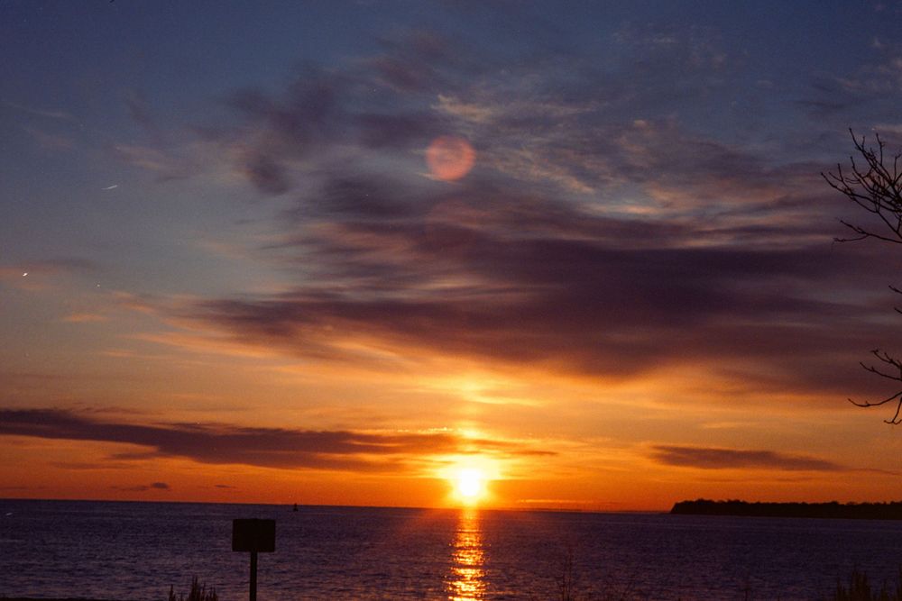 Vibrant orange and purple sunset over water with glowing horizon.