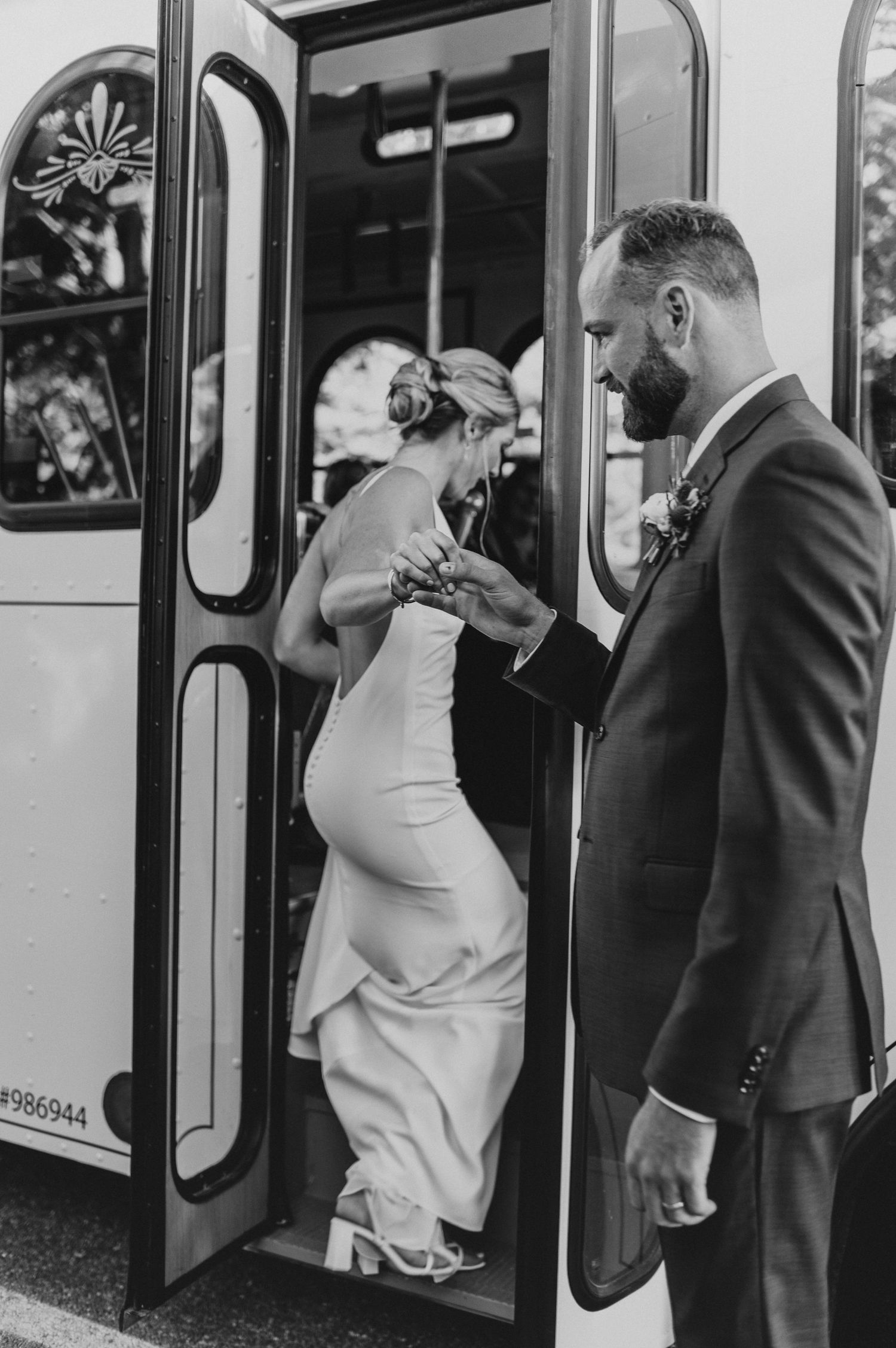 Black and white image of a bride stepping into a trolley bus while groom assists.