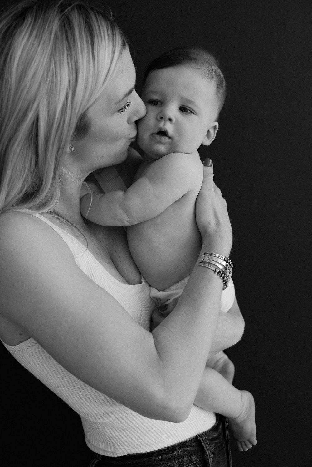 Black and white portrait of tender mother-child moment against dark background.
