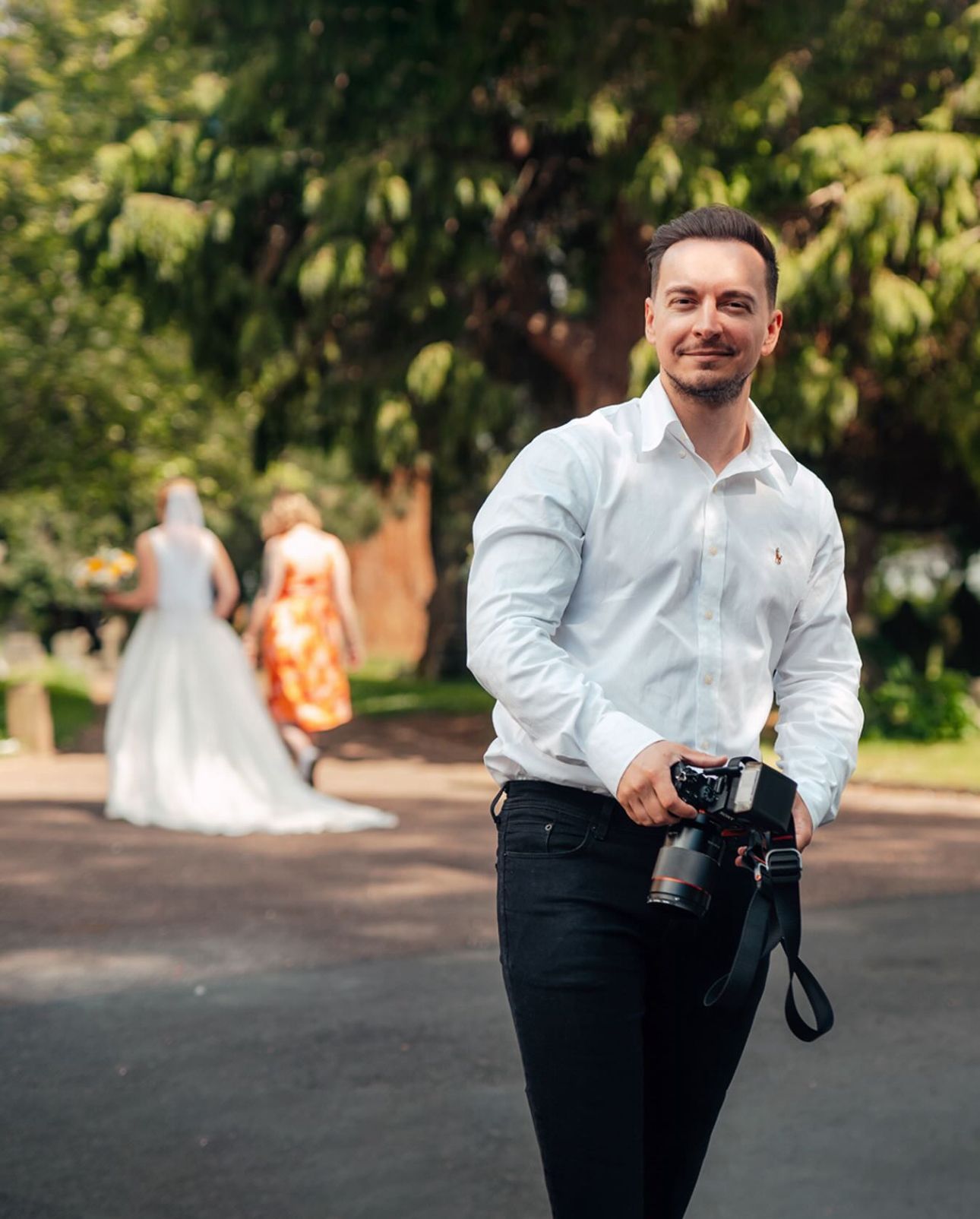 Professional photographer in white shirt and black pants captures wedding moments in a garden setting.
