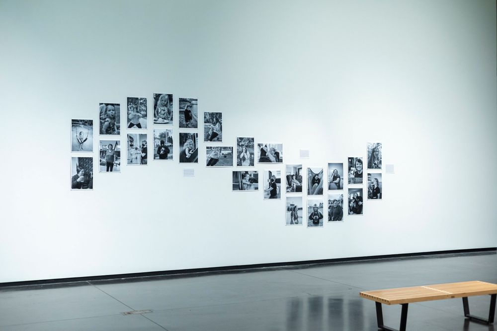 Black and white photographs arranged in a curved pattern on a stark white gallery wall.