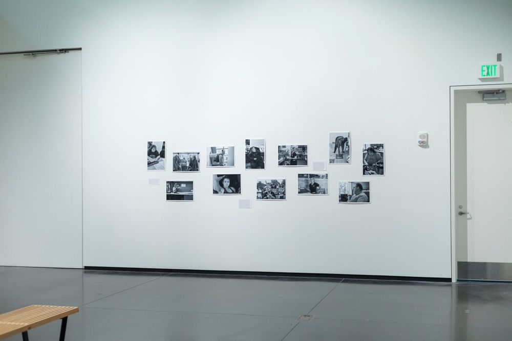 Gallery space with black and white photographs mounted in a horizontal line on a white wall.