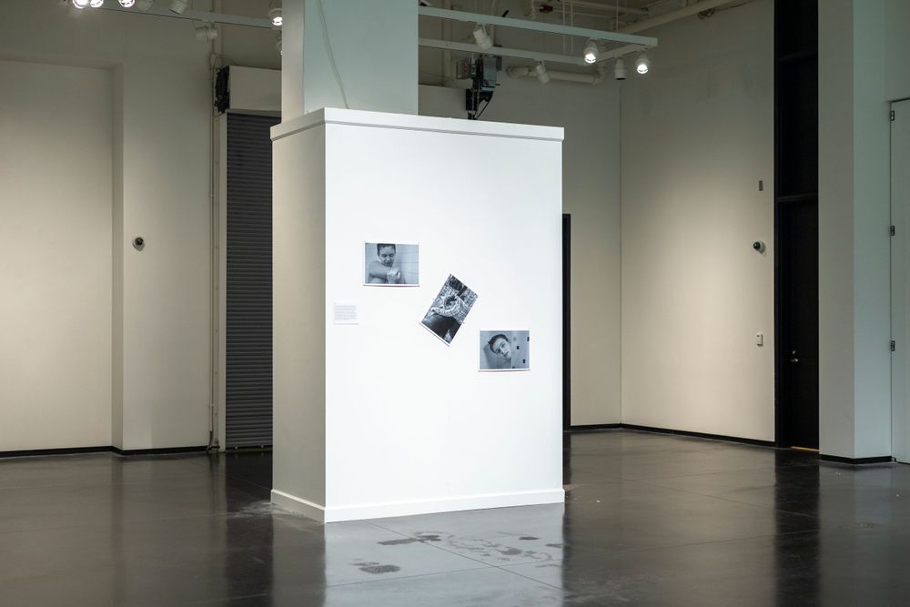 Minimalist gallery installation with three black and white photographs on a white column.