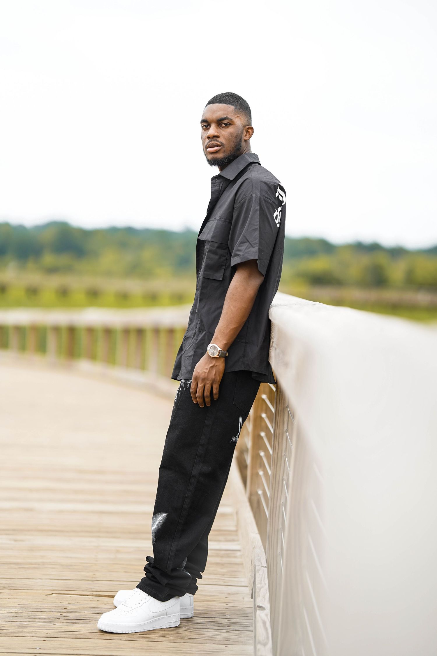 Casual fashion photography series showing model leaning against white railing on outdoor boardwalk.