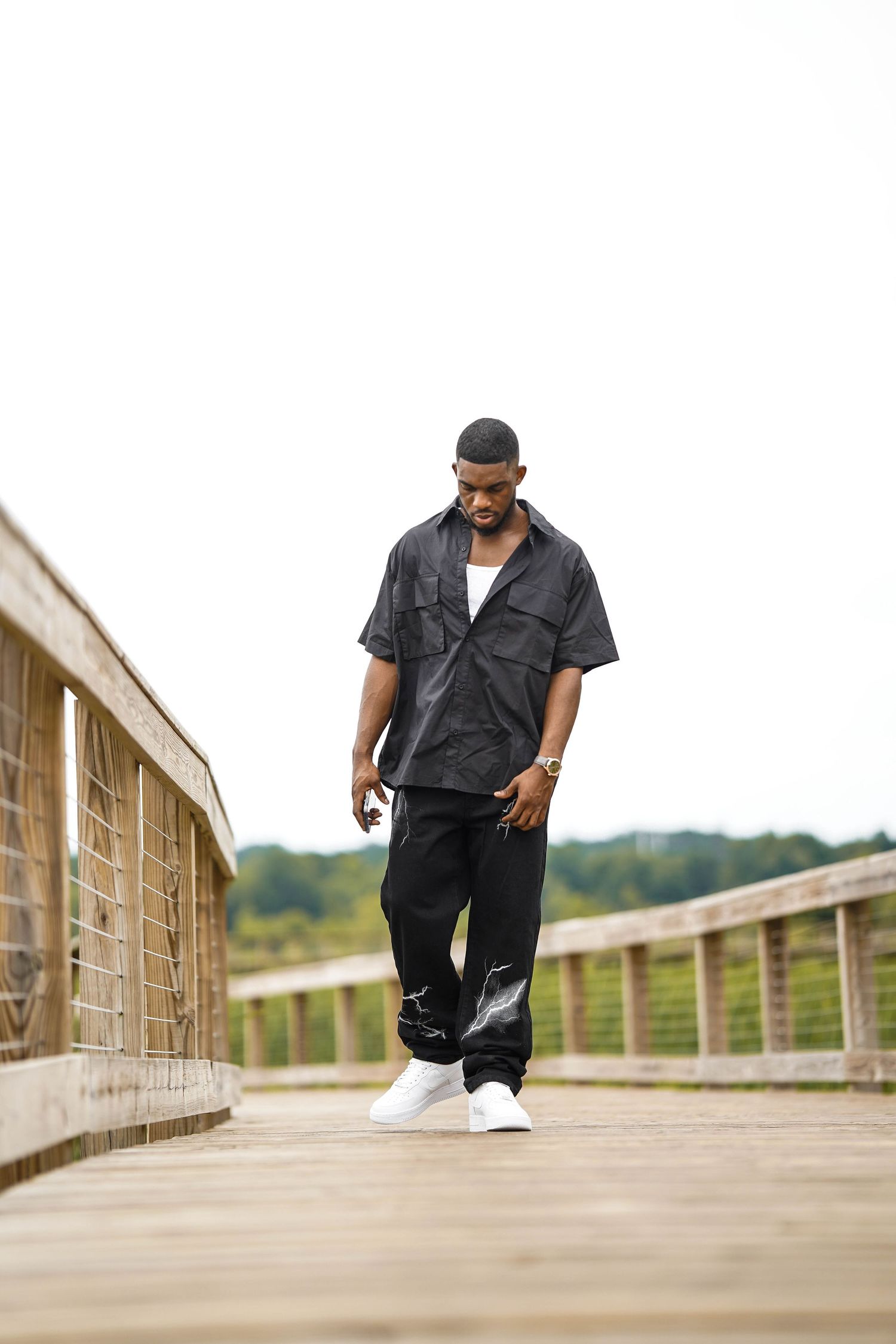 Urban fashion shoot featuring model in black streetwear walking along wooden boardwalk.