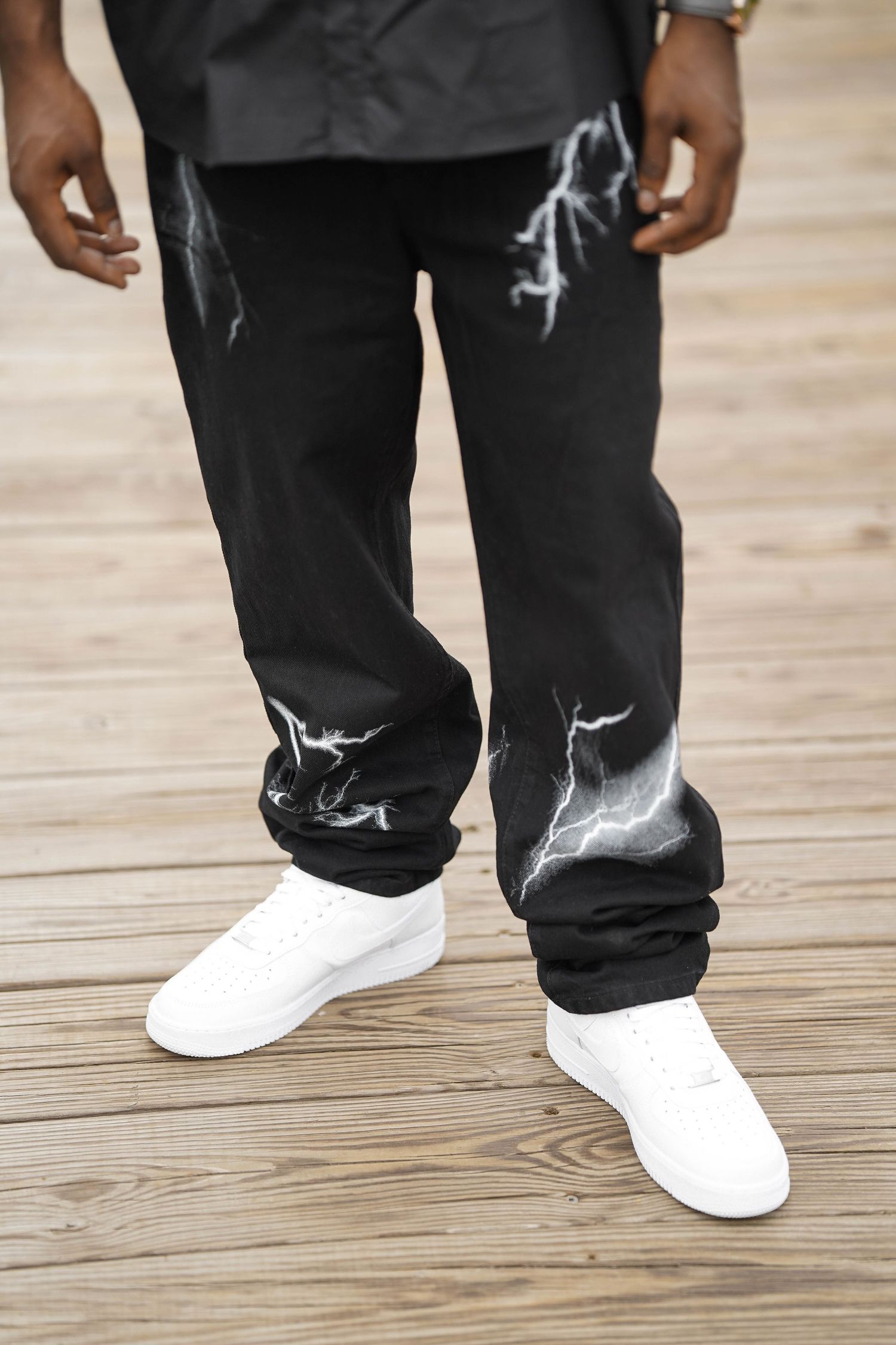 Close-up of model wearing black pants and white sneakers on wooden boardwalk.