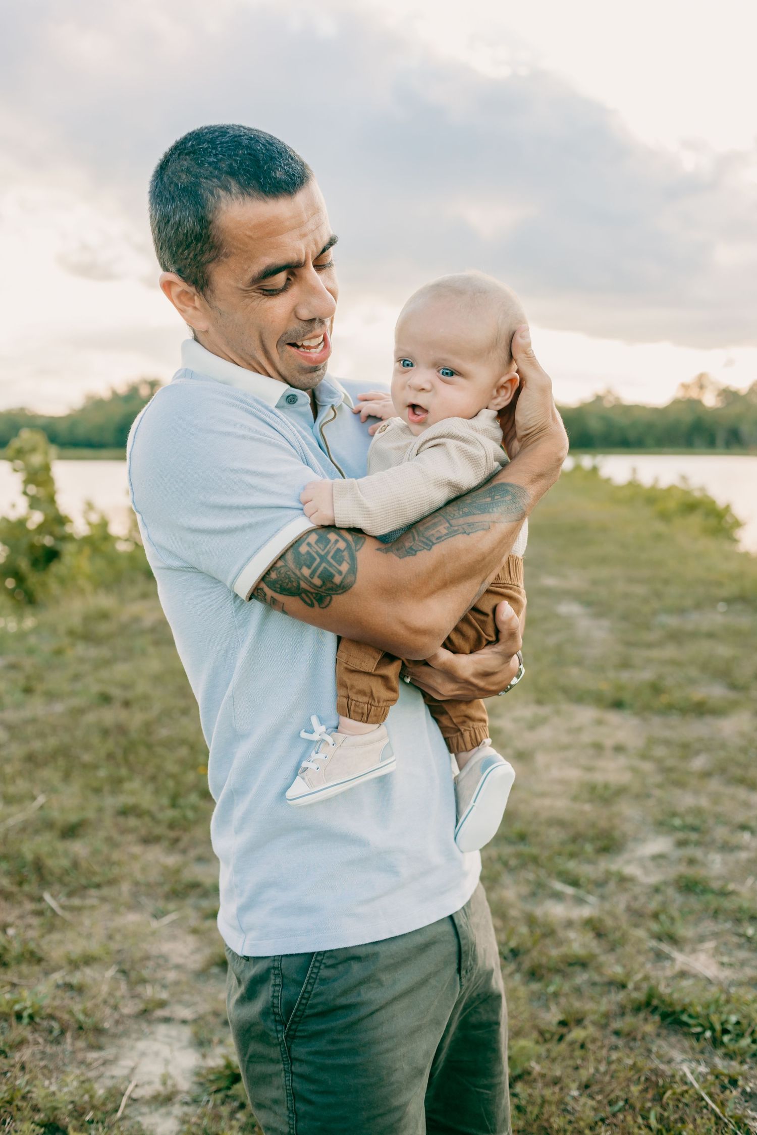 Tender moment between adult and baby outdoors during golden hour near water.