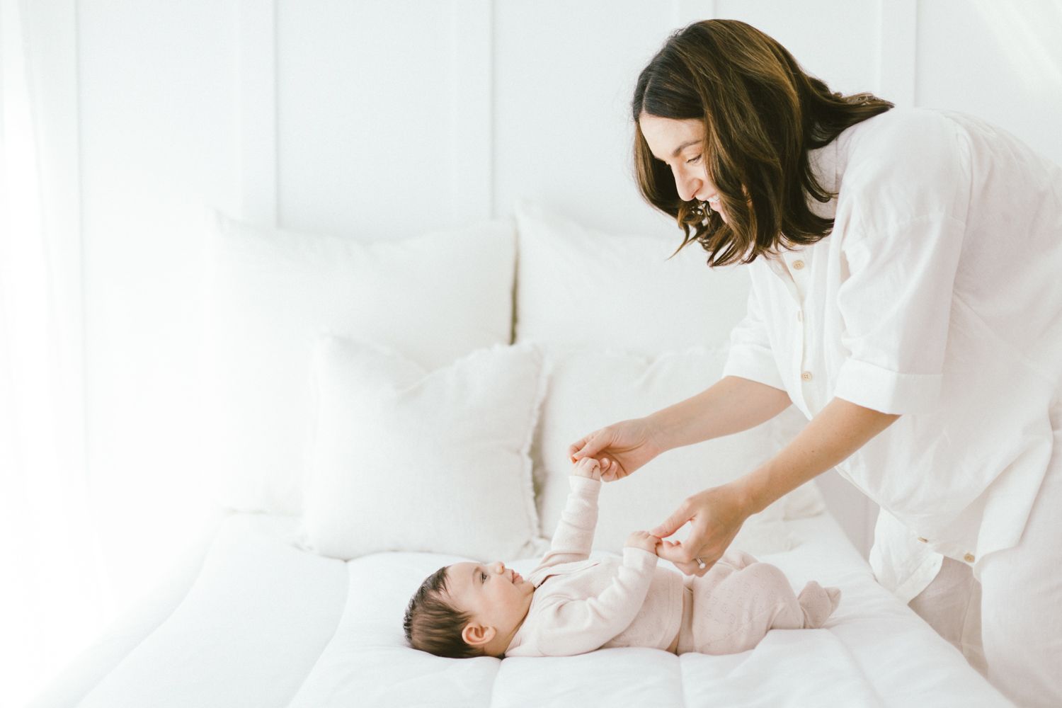 Caregiver in white tending to baby dressed in light beige on white bed.