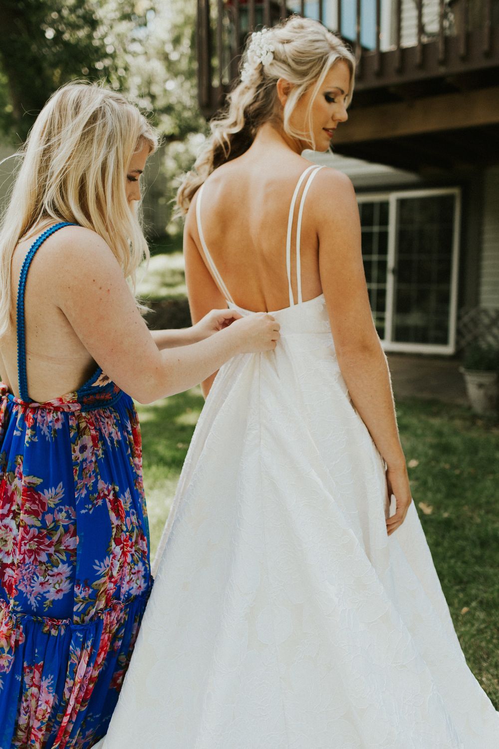 Bridesmaids in blue floral dresses help adjust a bride's wedding gown train.