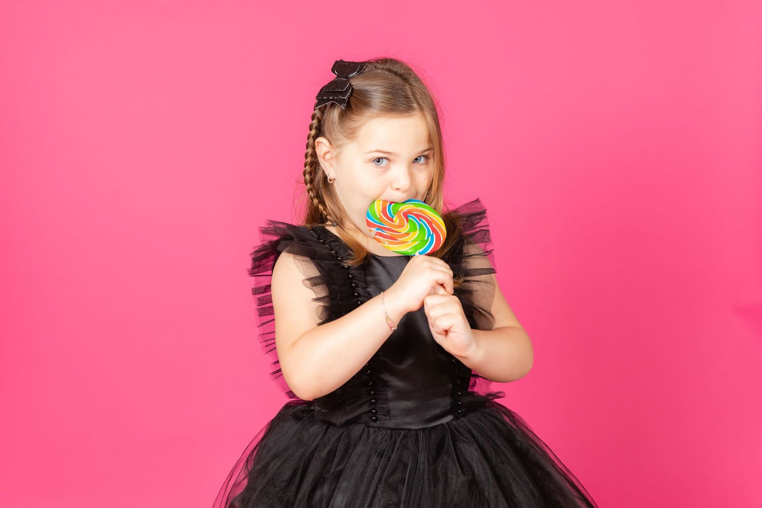 girl in black dress with bright lollipop on savage tulip pink backdrop in studio in clayton new jersey Gloucester county