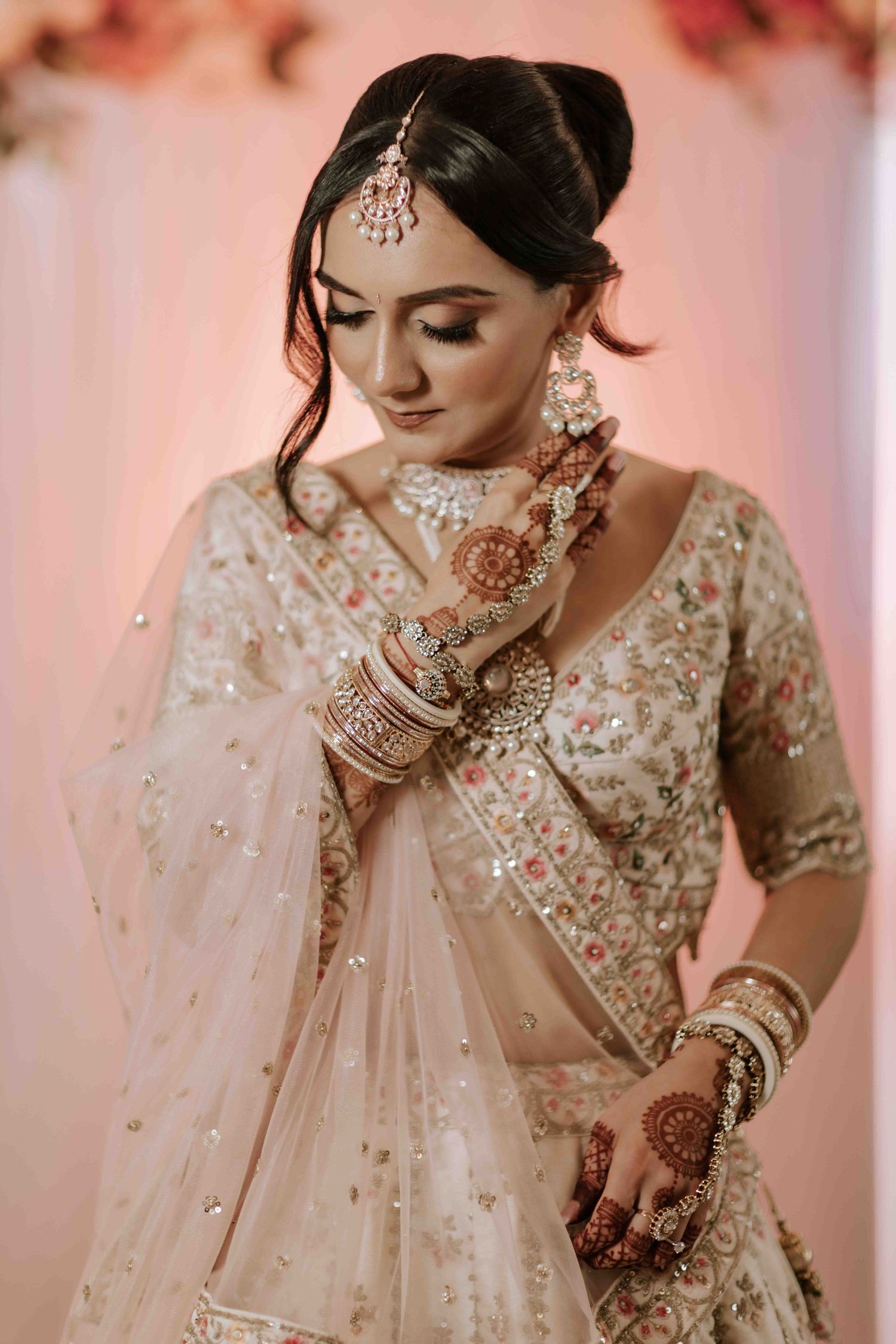 Close-up of bride wearing intricate Indian jewelry and henna details in pink-toned setting.