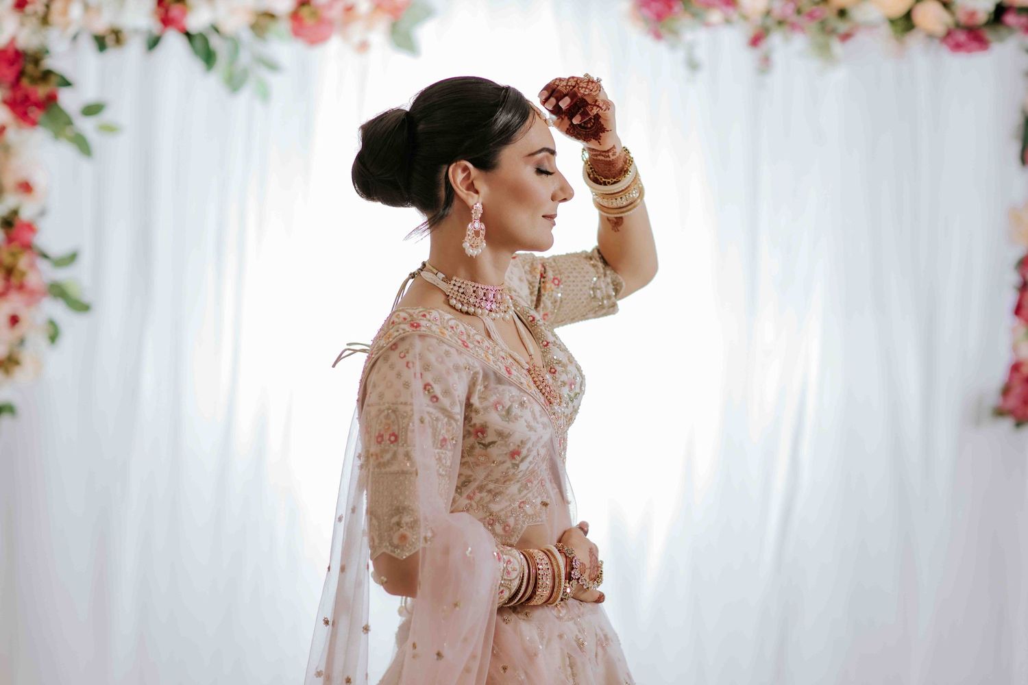 Bride in traditional Indian attire poses elegantly with floral decorations in the background.