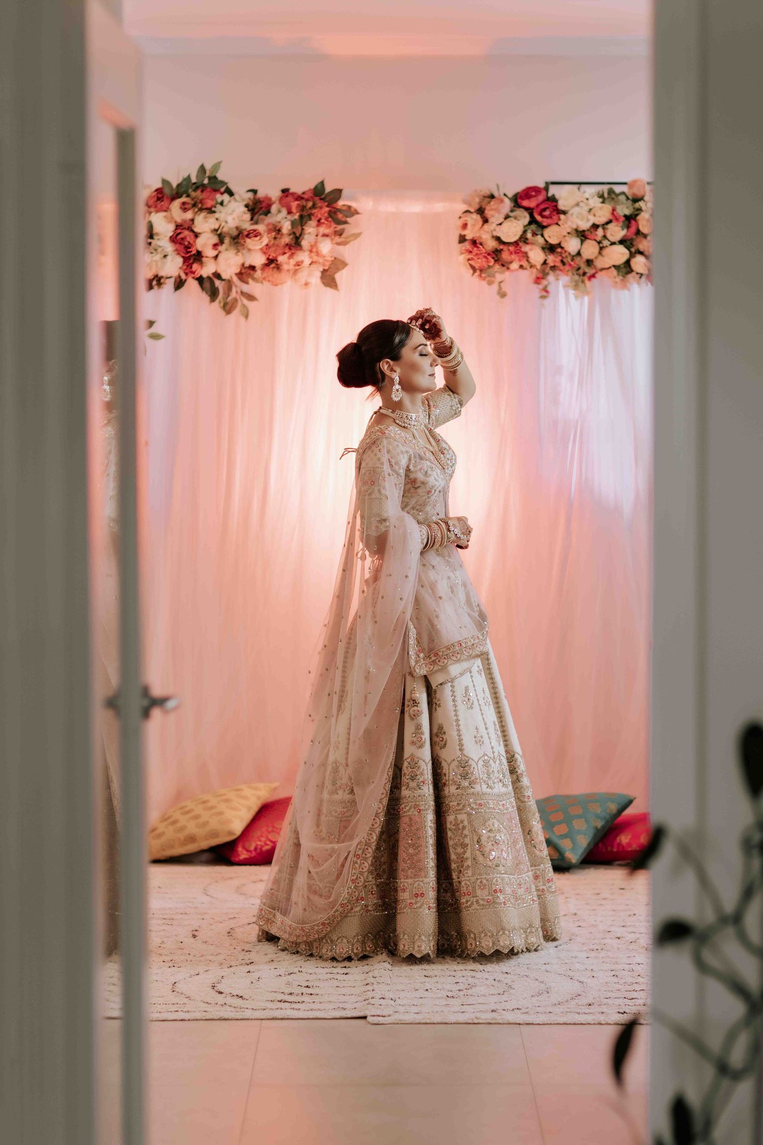 Full-length portrait of bride in embroidered lehenga with floral arch decorations.
