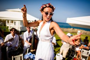 Woman in white dress dances joyfully at outdoor beach celebration.