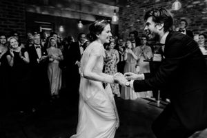A couple shares a dance moment surrounded by guests in an industrial brick venue.