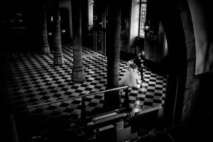 Black and white photo of a dramatic checkered floor interior with arched columns and dramatic lighting.