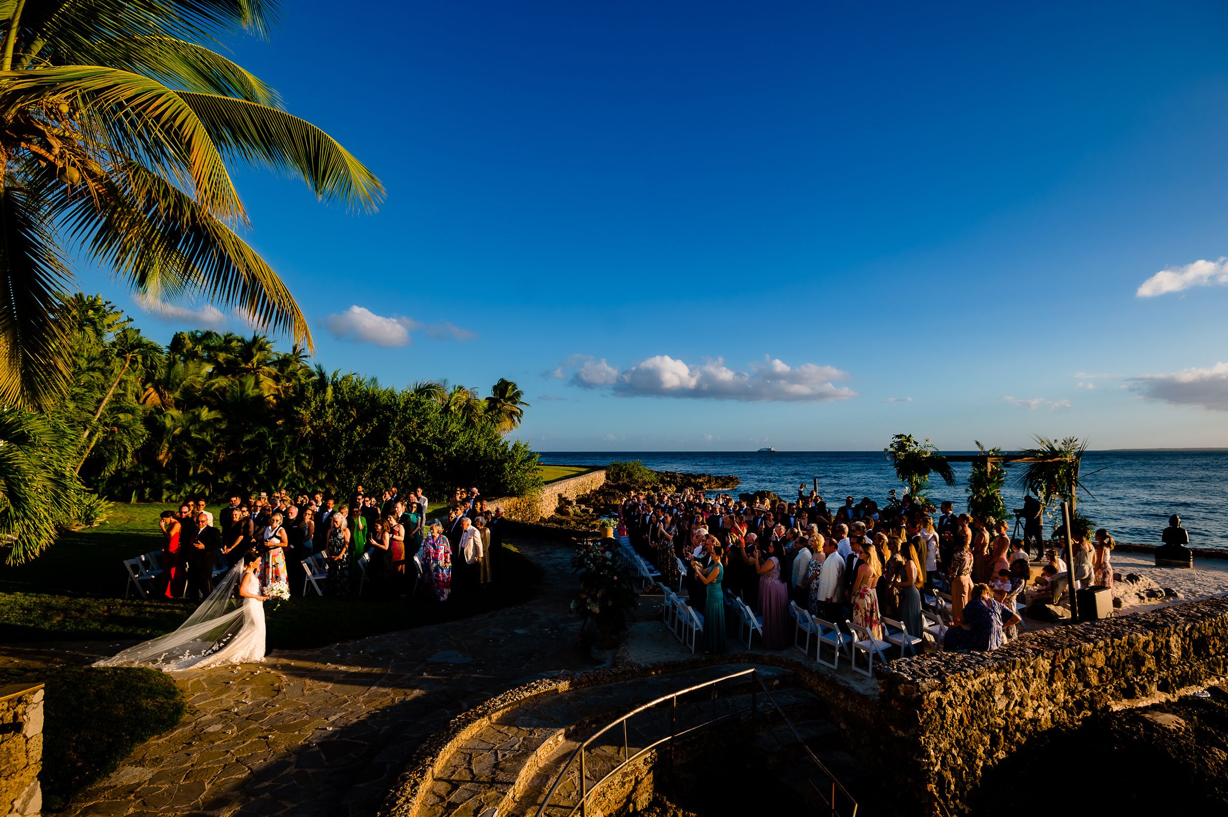 Scenic oceanfront wedding ceremony with guests gathered on a tropical cliff overlooking the sea.