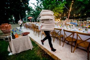 Person carrying stacked chairs while running across an outdoor wedding reception setup.