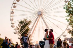 A couple shares a romantic moment in front of a large ferris wheel at sunset.