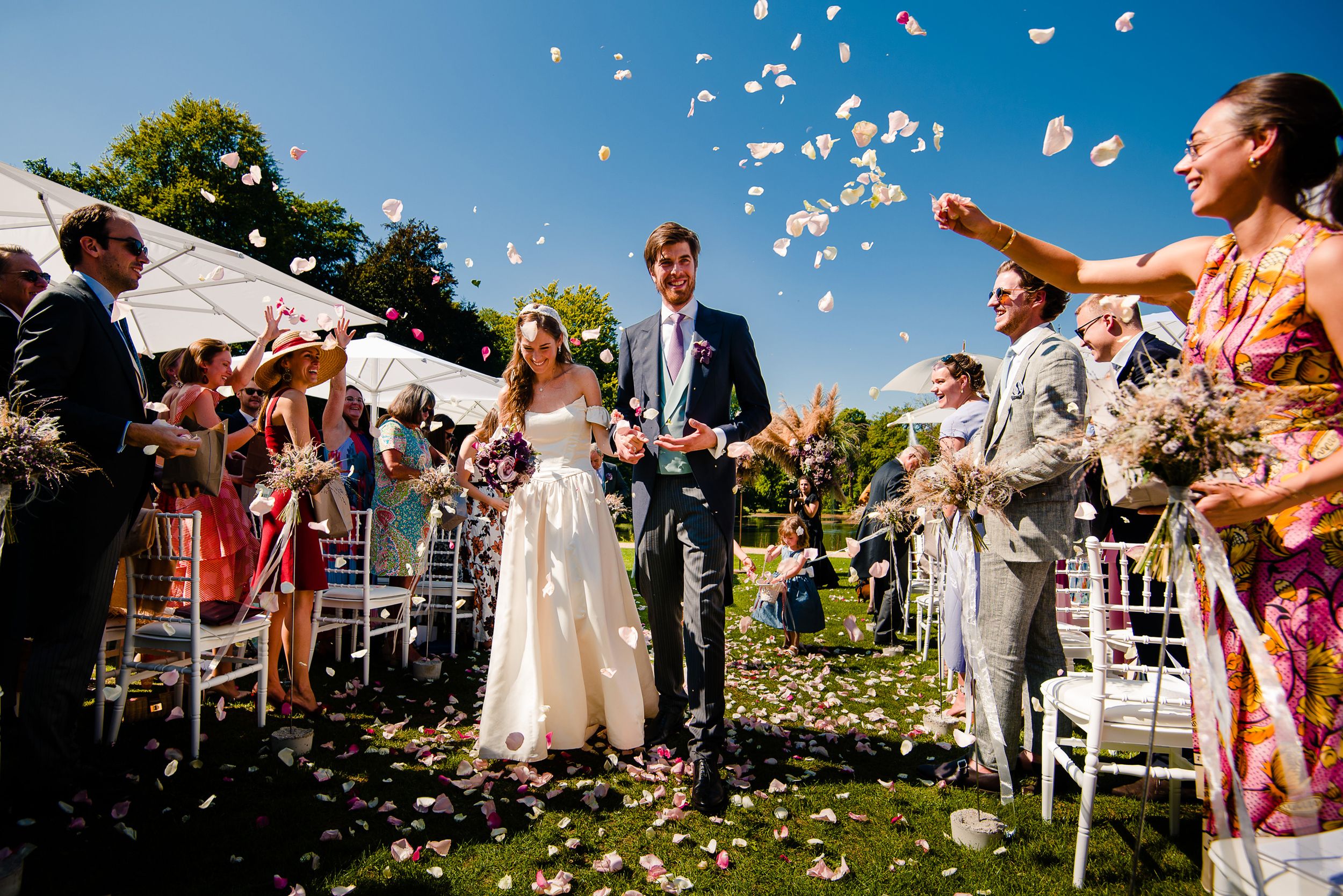 Celebrating newlyweds walk down the aisle while guests shower them with white flower petals.