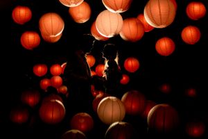 Silhouettes of couple surrounded by glowing orange paper lanterns at night.