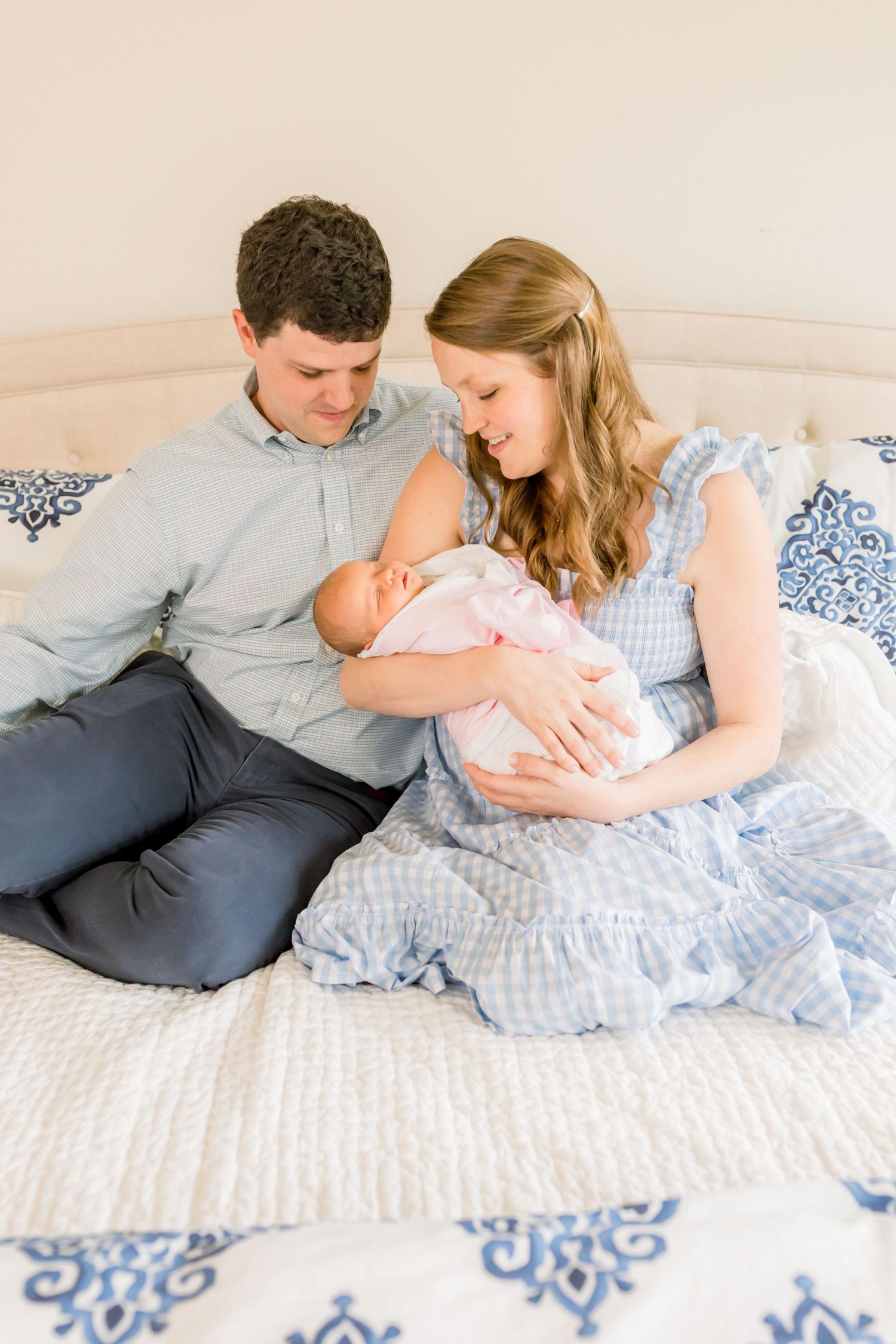 Parents share an intimate moment with their newborn baby on a bed with blue patterned bedding.