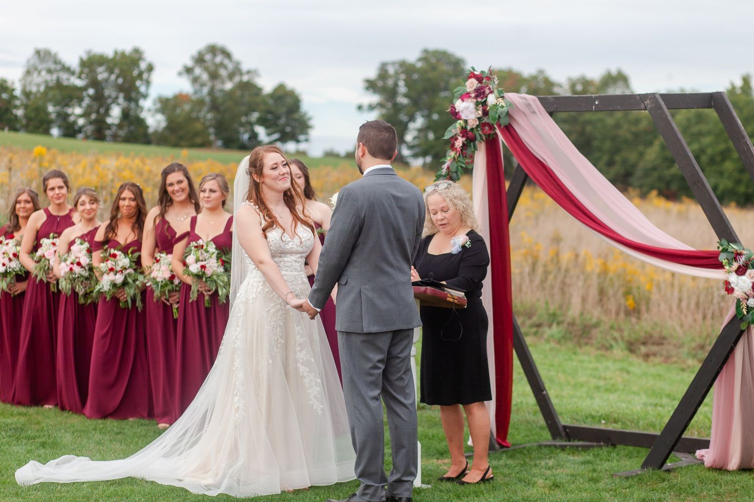 An outdoor wedding celebration with burgundy bridesmaids and elegant floral decorations.