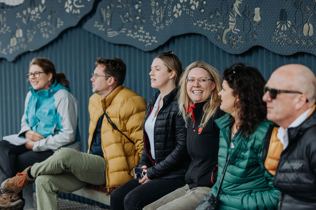 People sit together on wooden benches during an outdoor educational session in natural surroundings.
