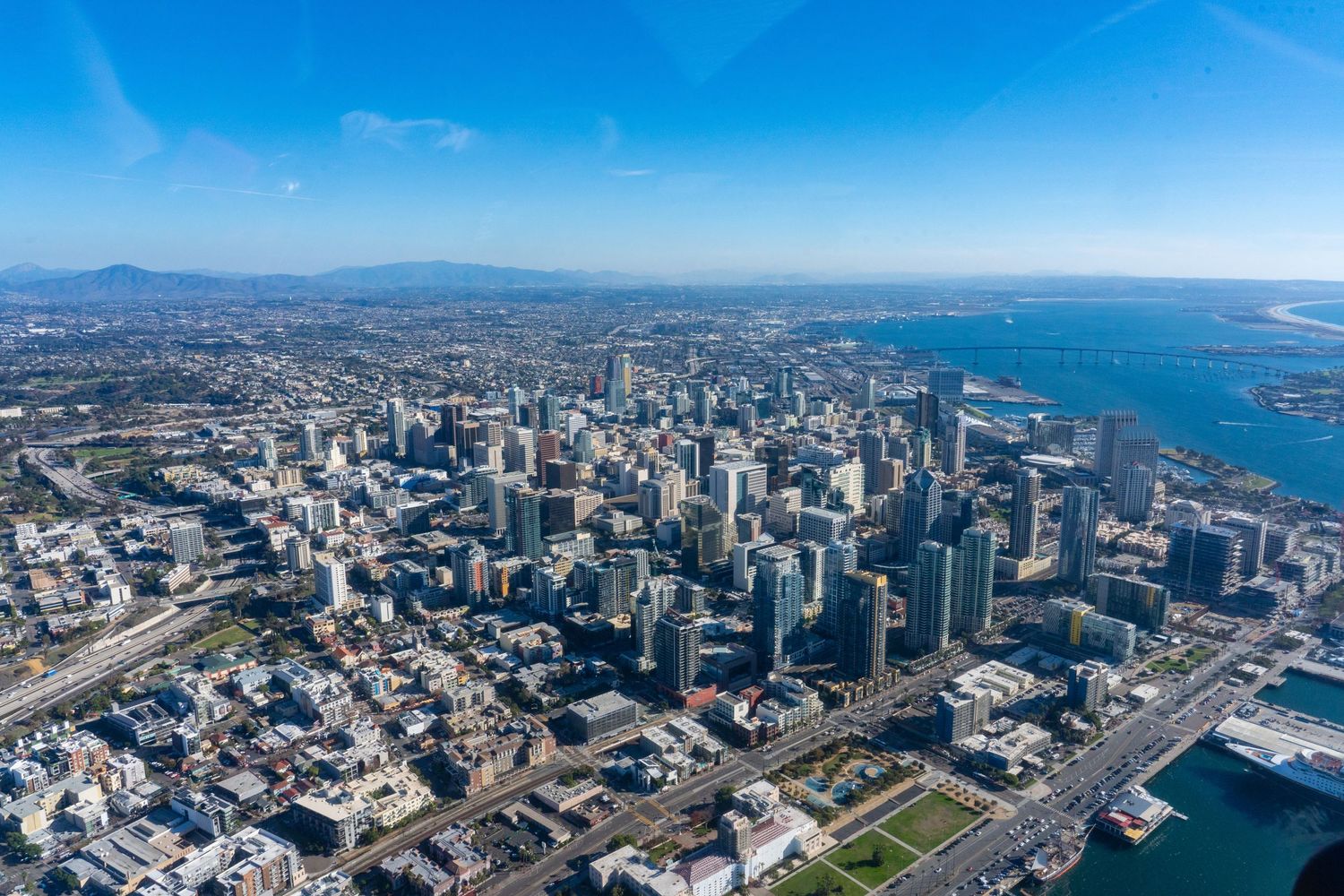 Aerial view of the downtown San Diego skyline, high-rise buildings, and the San Diego Bay waterfront on a sunny day.