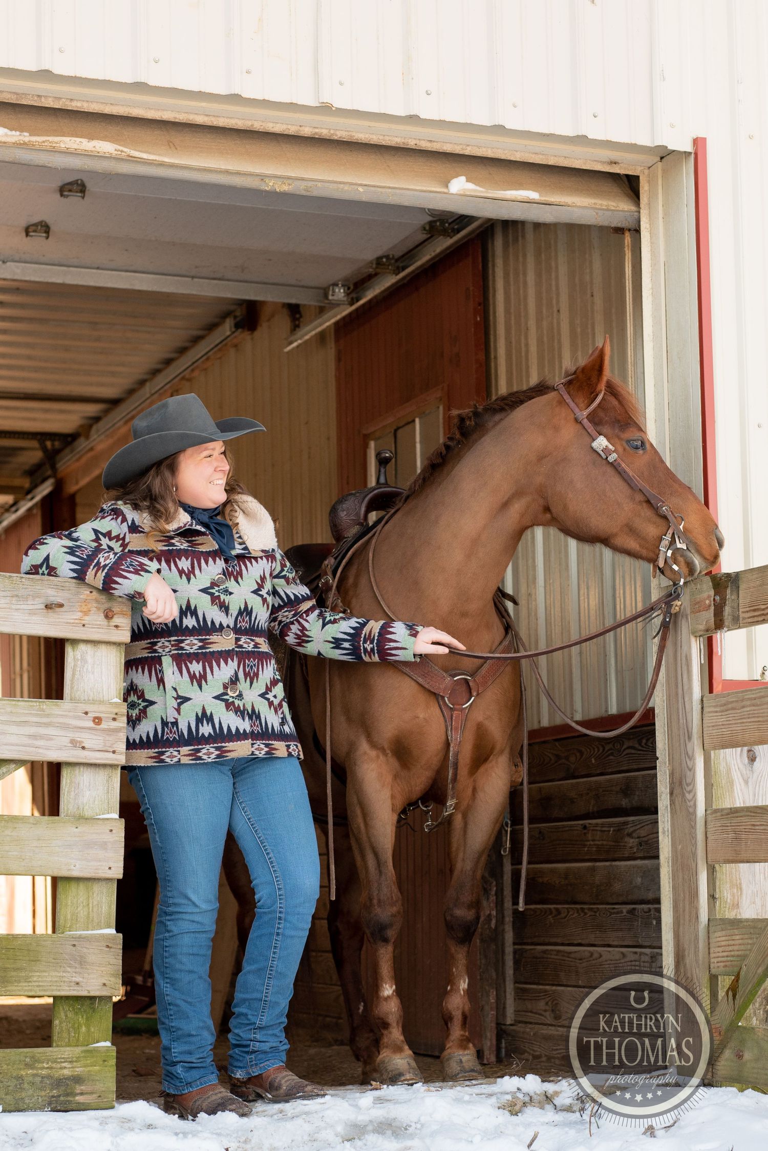Beautiful chestnut horse in stable with handler wearing patterned sweater and cowboy hat.