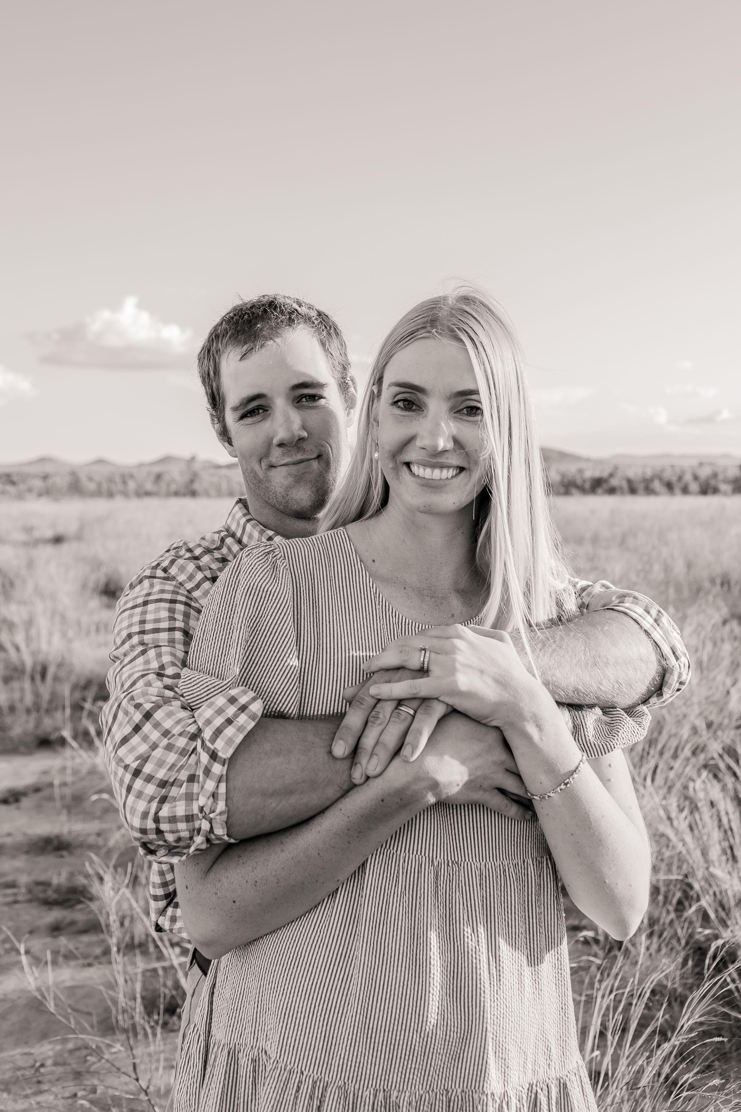 A couple embraces in a field with mountains in the background during a romantic photoshoot.