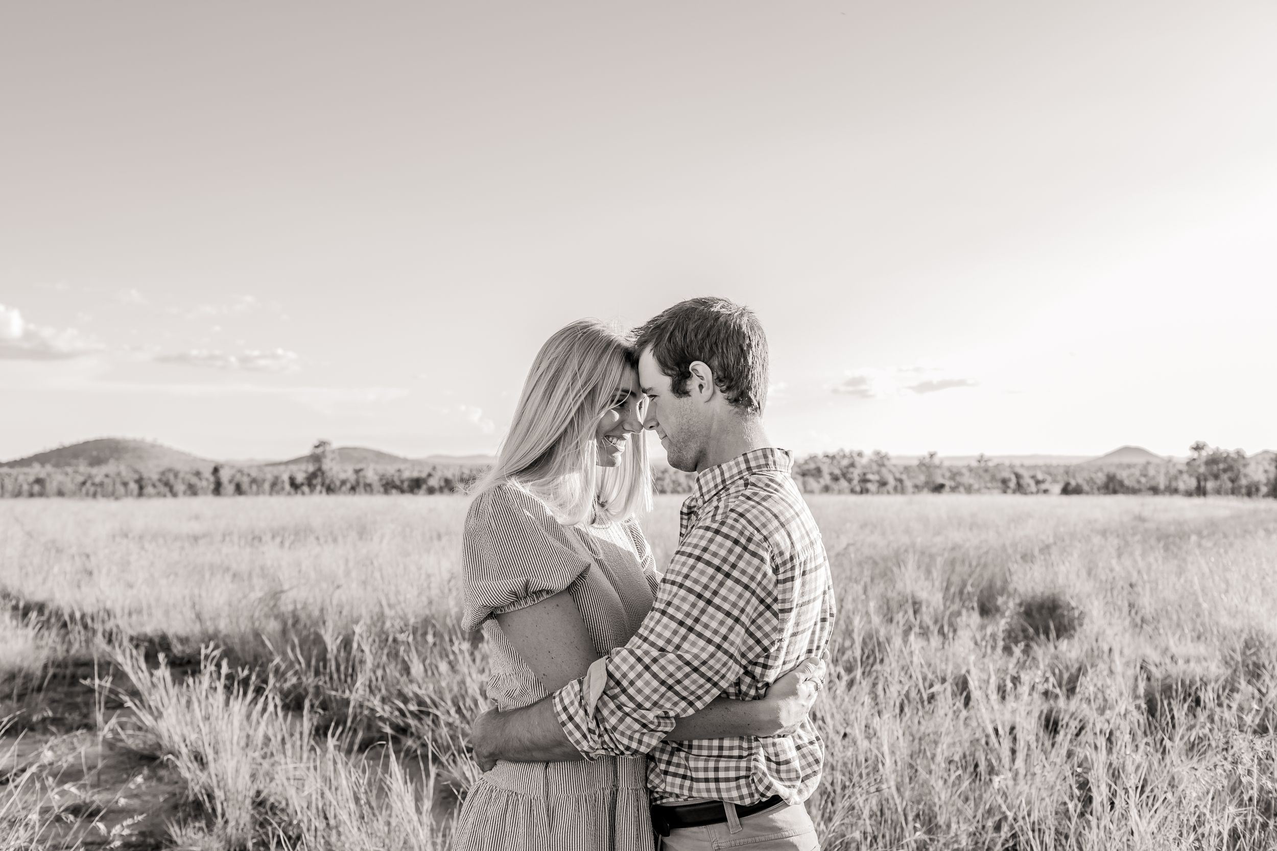 A tender moment captured in black and white as a couple embraces in a grassy field.