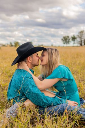 A romantic couple shares an intimate moment while sitting in tall grass during sunset.