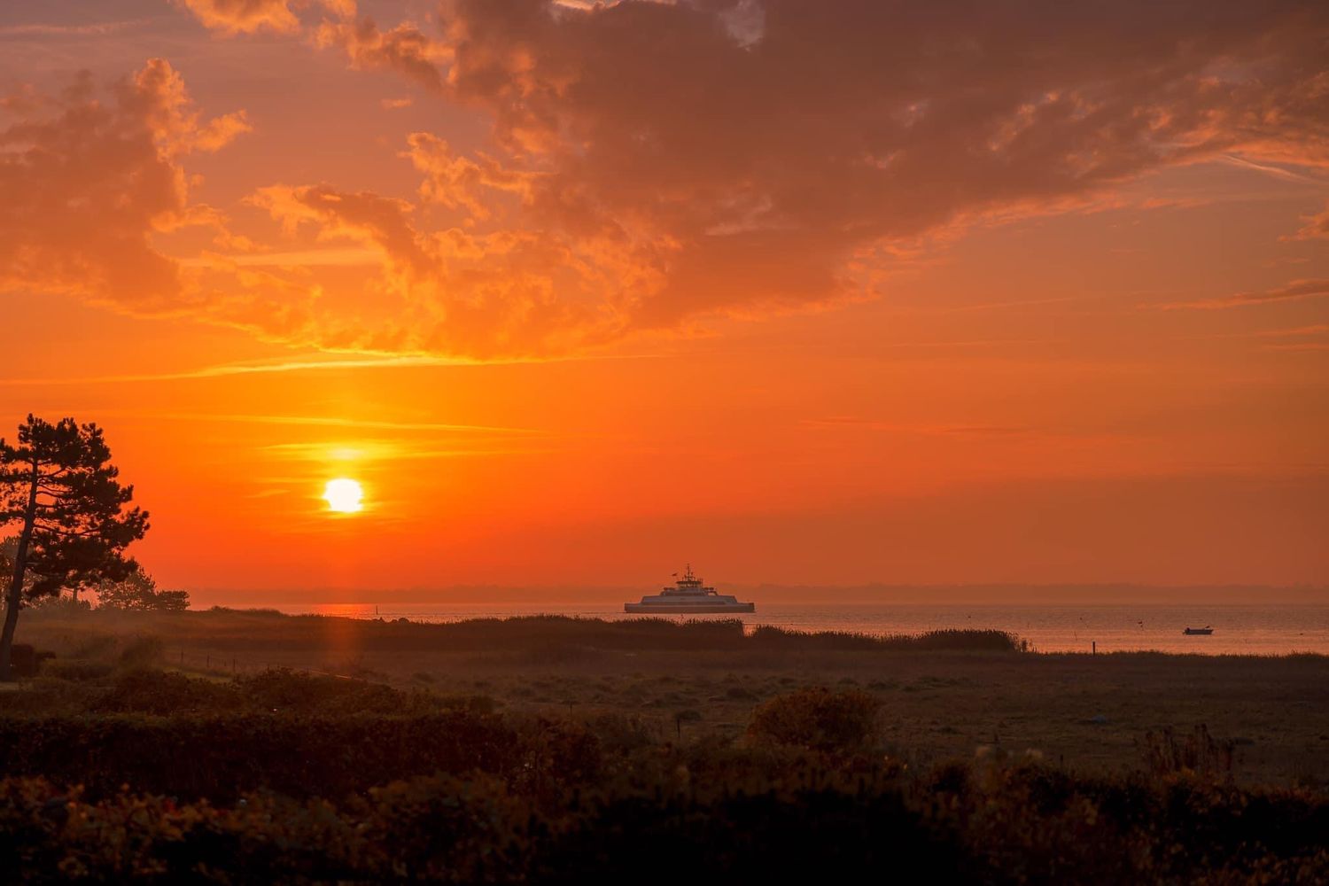 Stunning orange and red sunset over a silhouetted landscape with dramatic clouds.