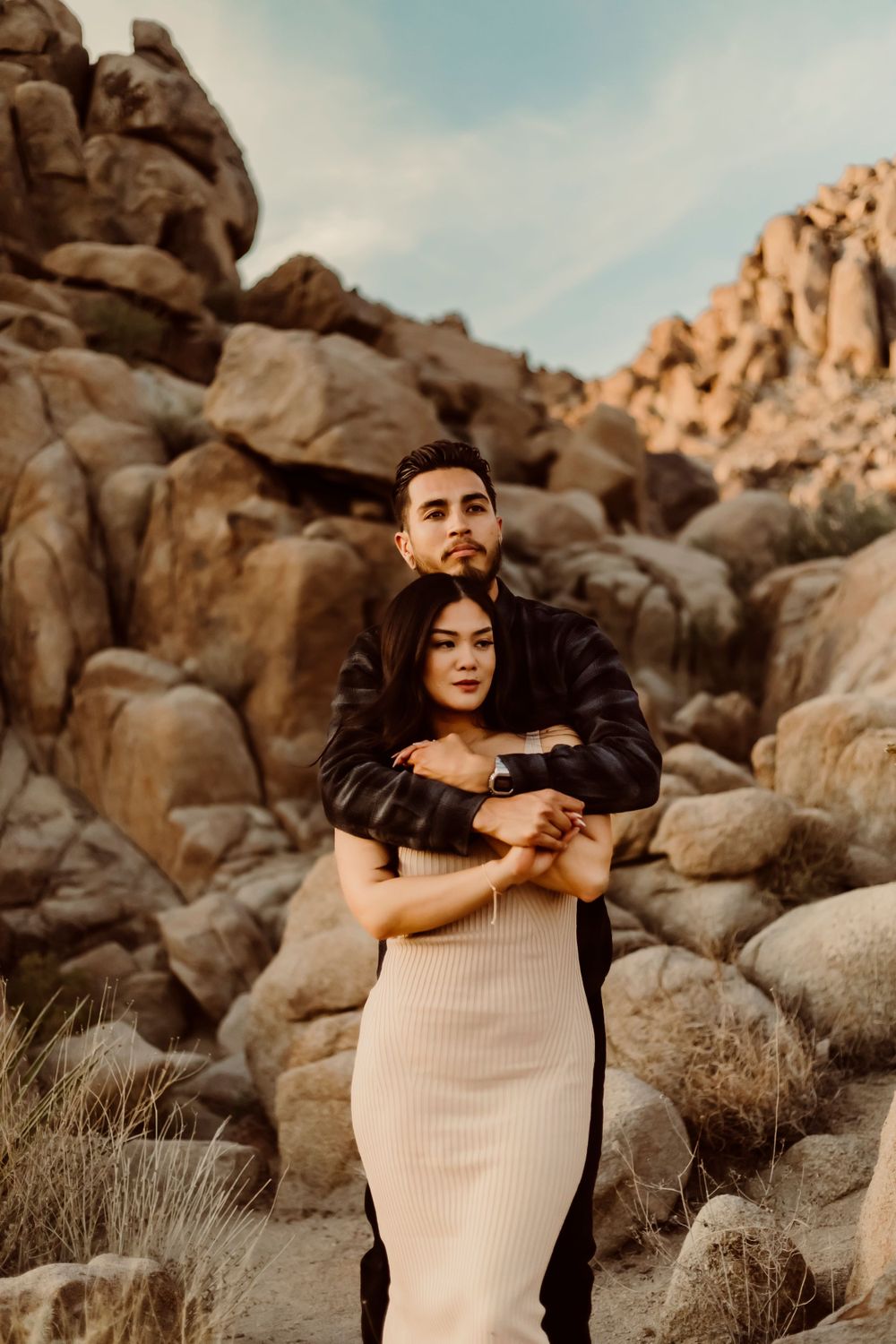 A couple embraces for Engagement photography in the large desert rock formations at sunset in Joshua Tree California