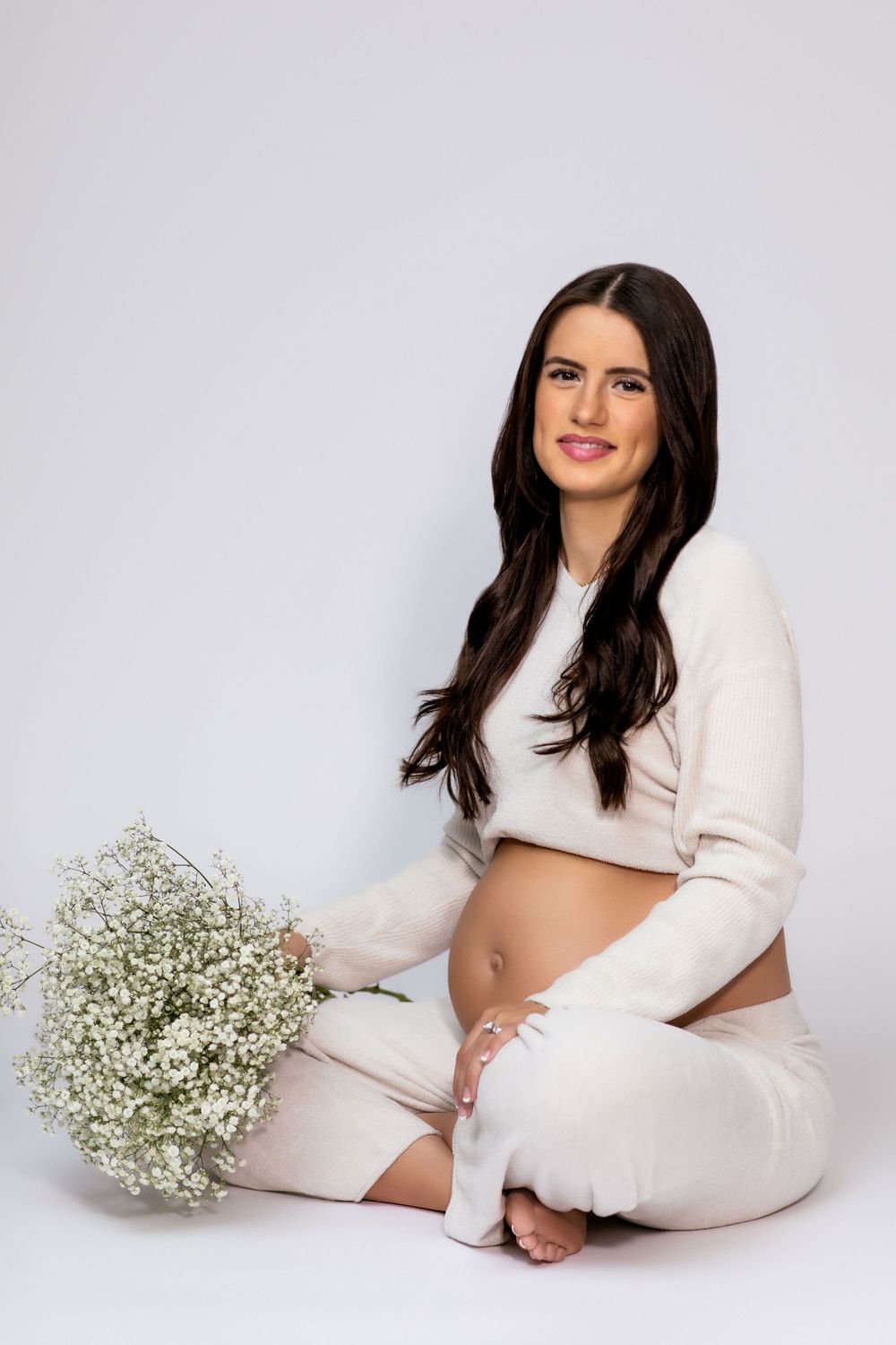 Maternity portrait featuring woman in white outfit holding baby's breath flowers.