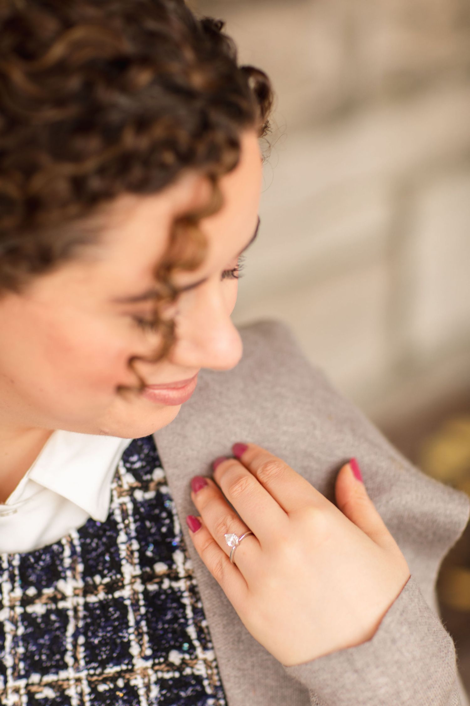 A close-up shot showing a sparkling engagement ring on a hand against a gray coat.