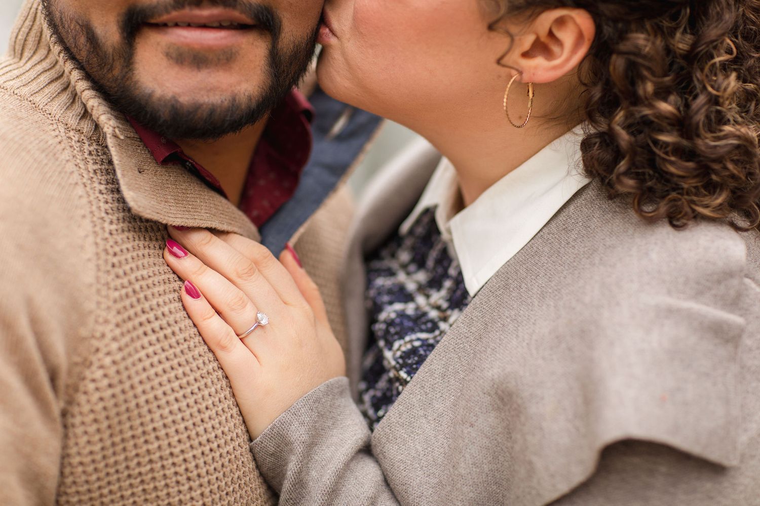 An intimate close-up of a couple embracing, showing details of their autumn attire.