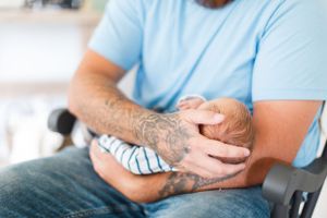 Tattooed hands gently holding small baby wearing striped outfit during a lifestyle newborn session in Springfield, MO.