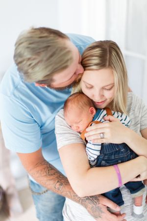 A tender family moment as parents embrace their newborn baby in casual attire against a bright background during a lifestyle newborn session
