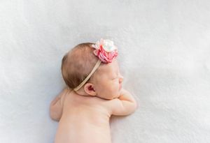 Sleeping newborn baby wearing a pink floral headband against white background taken during a lifestyle newborn session in Springfield, MO.