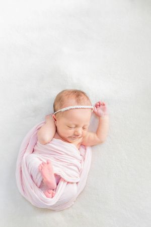 Peaceful sleeping newborn wrapped in soft pink fabric with dainty headband during a lifestyle newborn session in Springfield, MO.